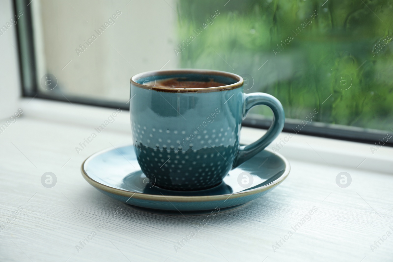 Photo of Cup of hot aromatic coffee on white wooden windowsill. Rainy weather