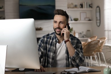 Man talking on phone while working with computer at table in home office