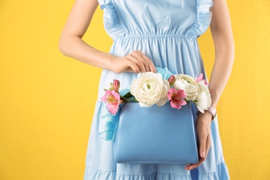 Photo of Woman holding elegant handbag with spring flowers on yellow background, closeup