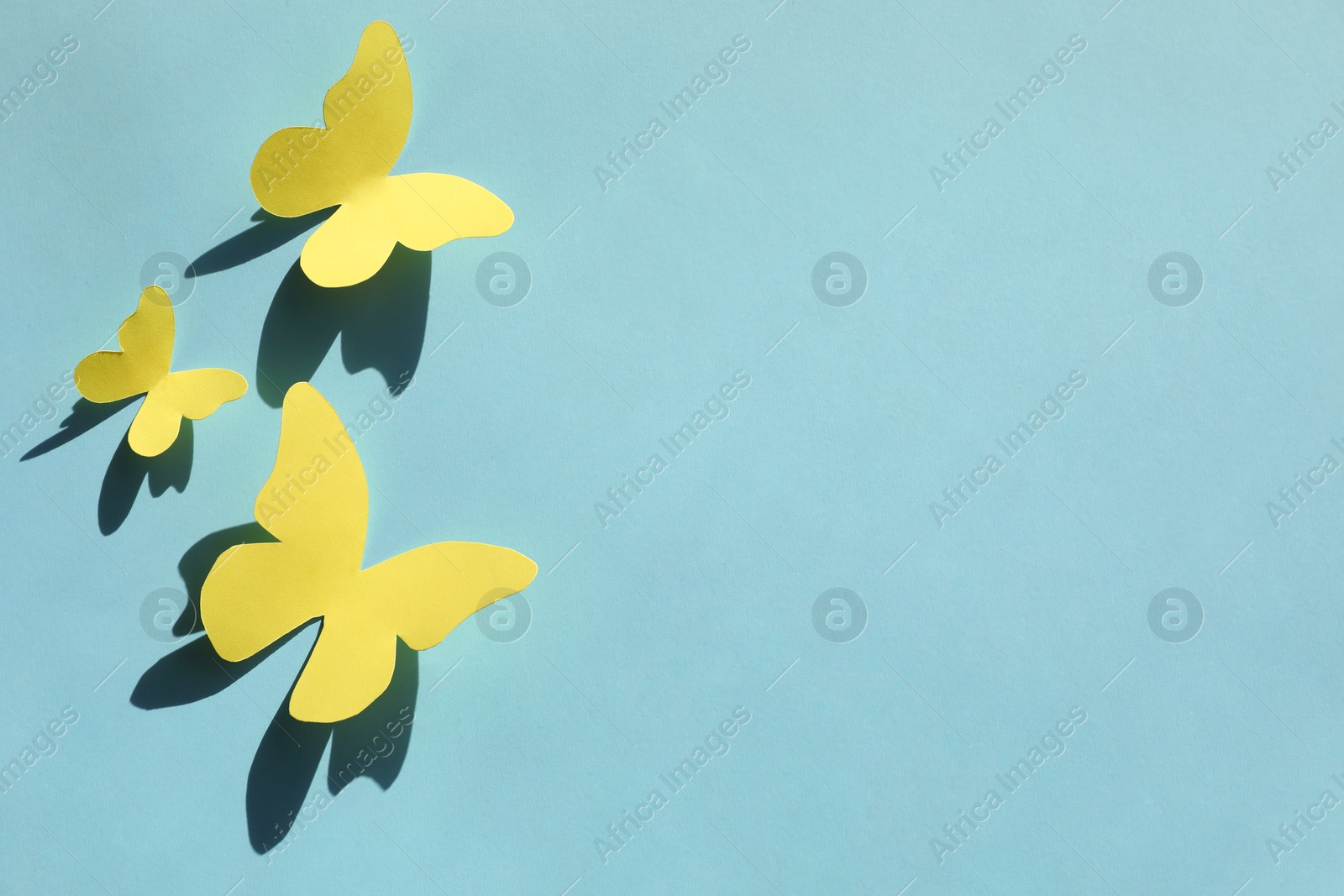 Photo of Yellow paper butterflies on turquoise background, top view. Space for text