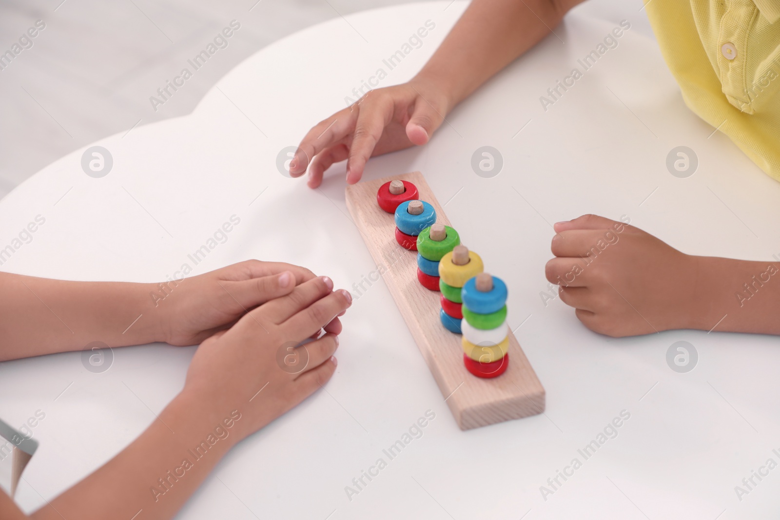 Photo of Little children playing with stacking and counting game at desk, closeup. Kindergarten activities for motor skills development