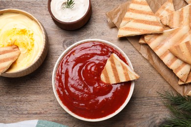 Photo of Sauce and pita chips on wooden table, flat lay