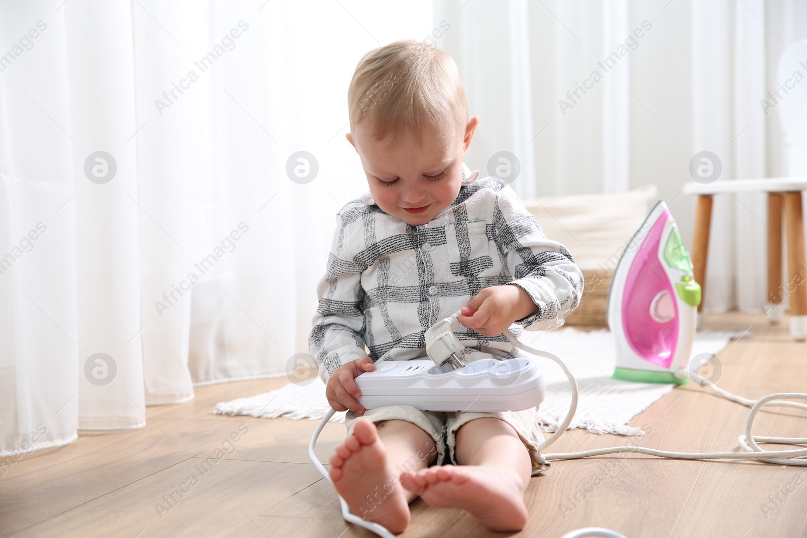 Photo of Little child playing with power strip and iron plug on floor at home. Dangerous situation