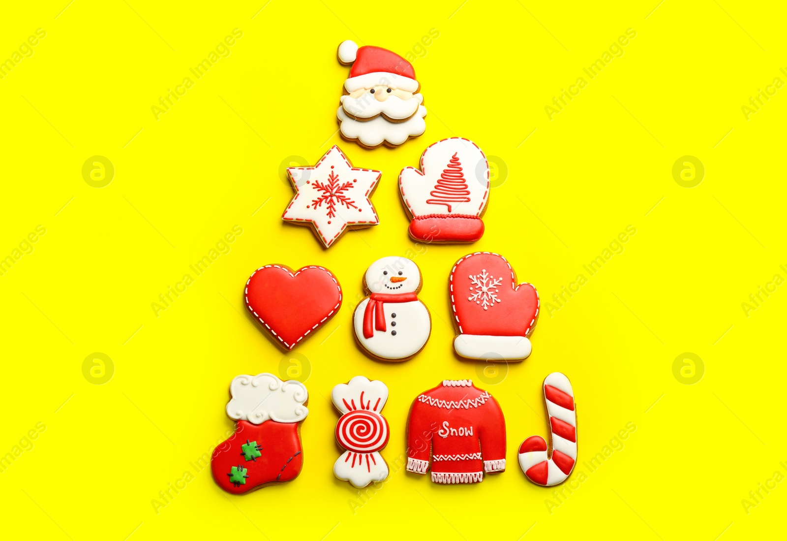 Photo of Delicious gingerbread cookies arranged in shape of Christmas tree on yellow background, flat lay