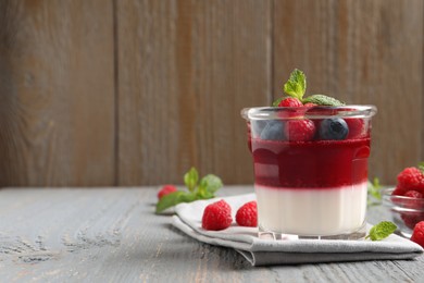 Photo of Delicious panna cotta with berries on grey wooden table. Space for text