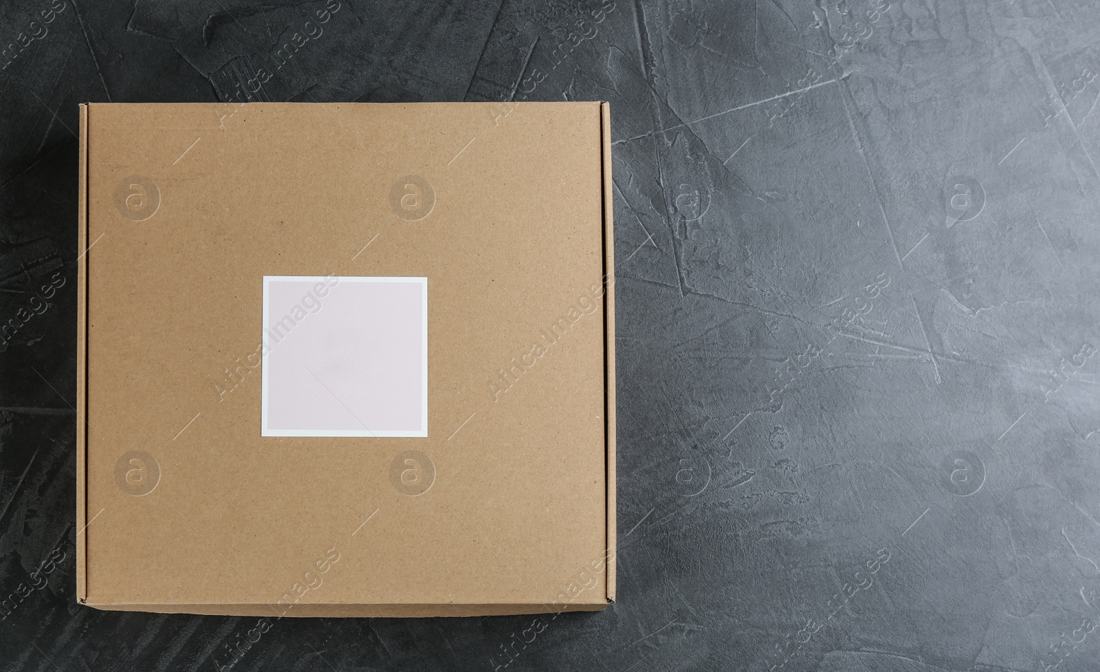 Photo of Closed cardboard box on grey stone table, top view. Space for text