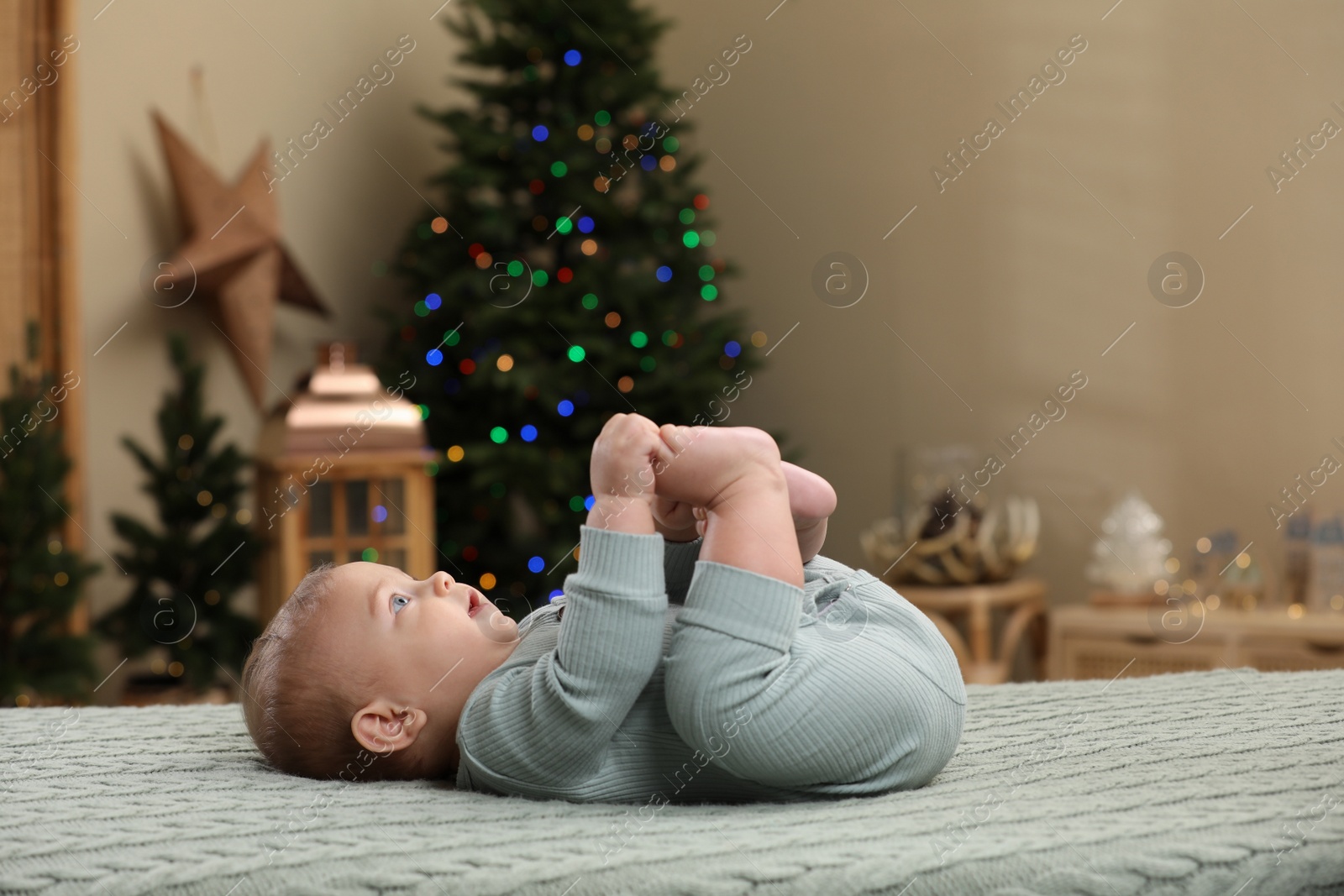 Photo of Cute little baby lying on knitted plaid in room decorated for Christmas. Winter holiday