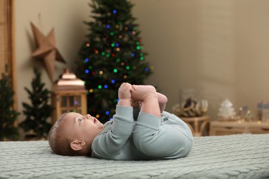 Cute little baby lying on knitted plaid in room decorated for Christmas. Winter holiday