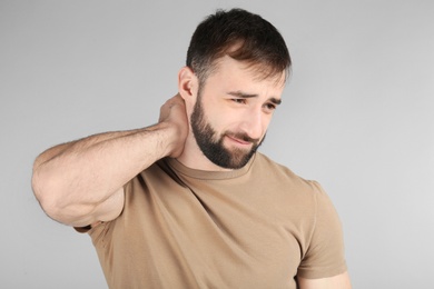 Young man suffering from neck pain on light background