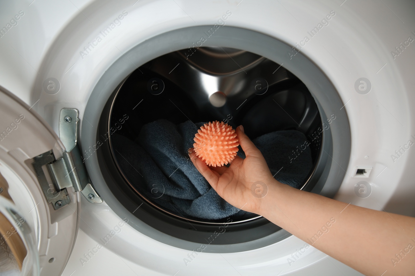 Photo of Woman putting dryer ball into washing machine, closeup