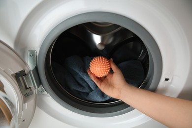 Photo of Woman putting dryer ball into washing machine, closeup