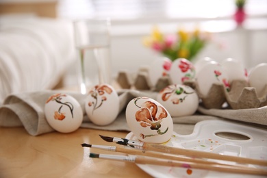 Photo of Beautifully painted Easter eggs and brushes on wooden table indoors