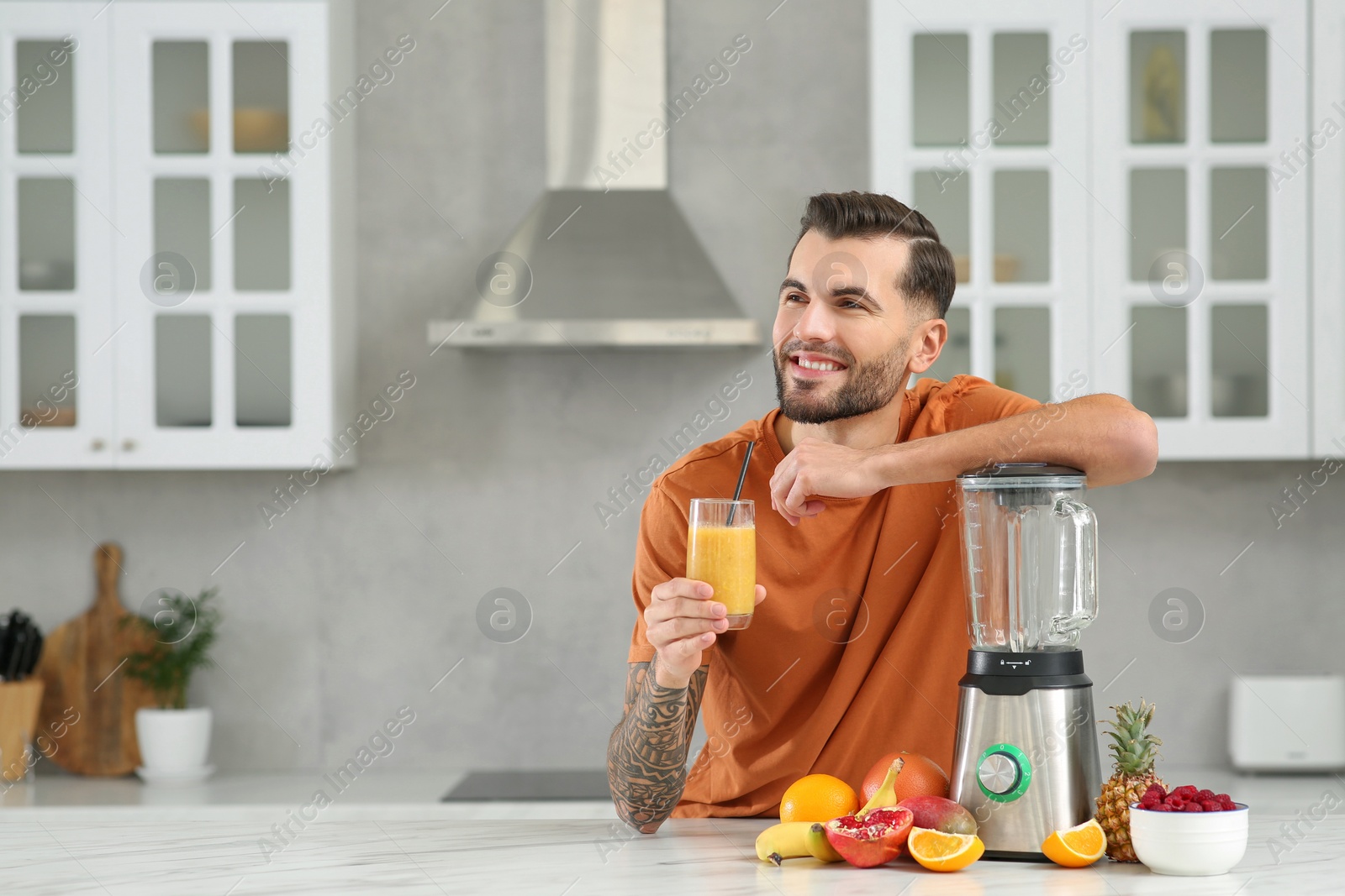 Photo of Handsome man with delicious smoothie at white marble table in kitchen. Space for text