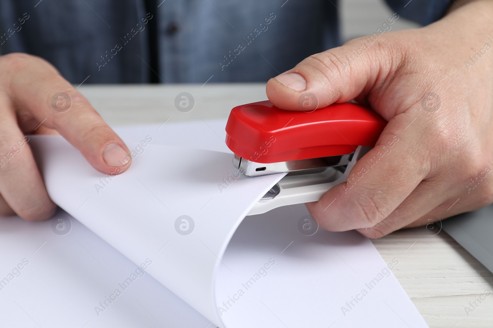 Photo of Man with papers using stapler at white table, closeup