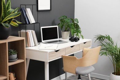 Photo of Workplace with laptop, stationery on desk and chair in home office