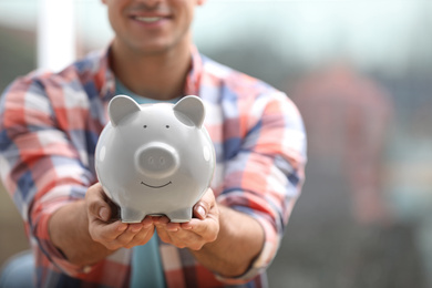 Man holding piggy bank against blurred background, closeup. Space for text