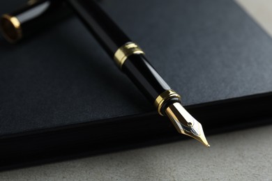 Photo of Beautiful fountain pen with ornate nib and black notebook on grey table, closeup