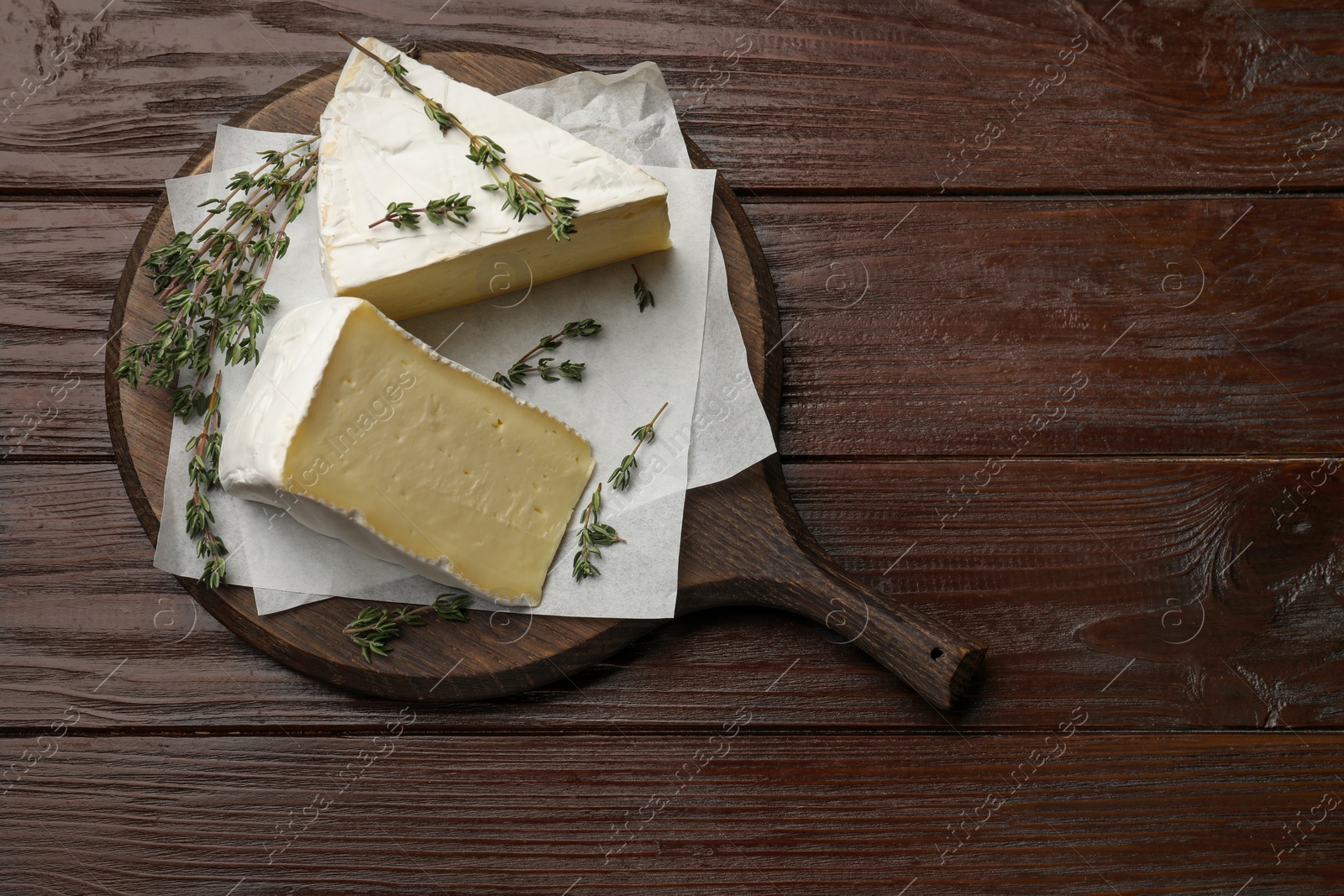 Photo of Board with pieces of tasty camembert cheese and thyme on wooden table, top view. Space for text