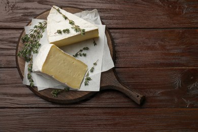 Board with pieces of tasty camembert cheese and thyme on wooden table, top view. Space for text