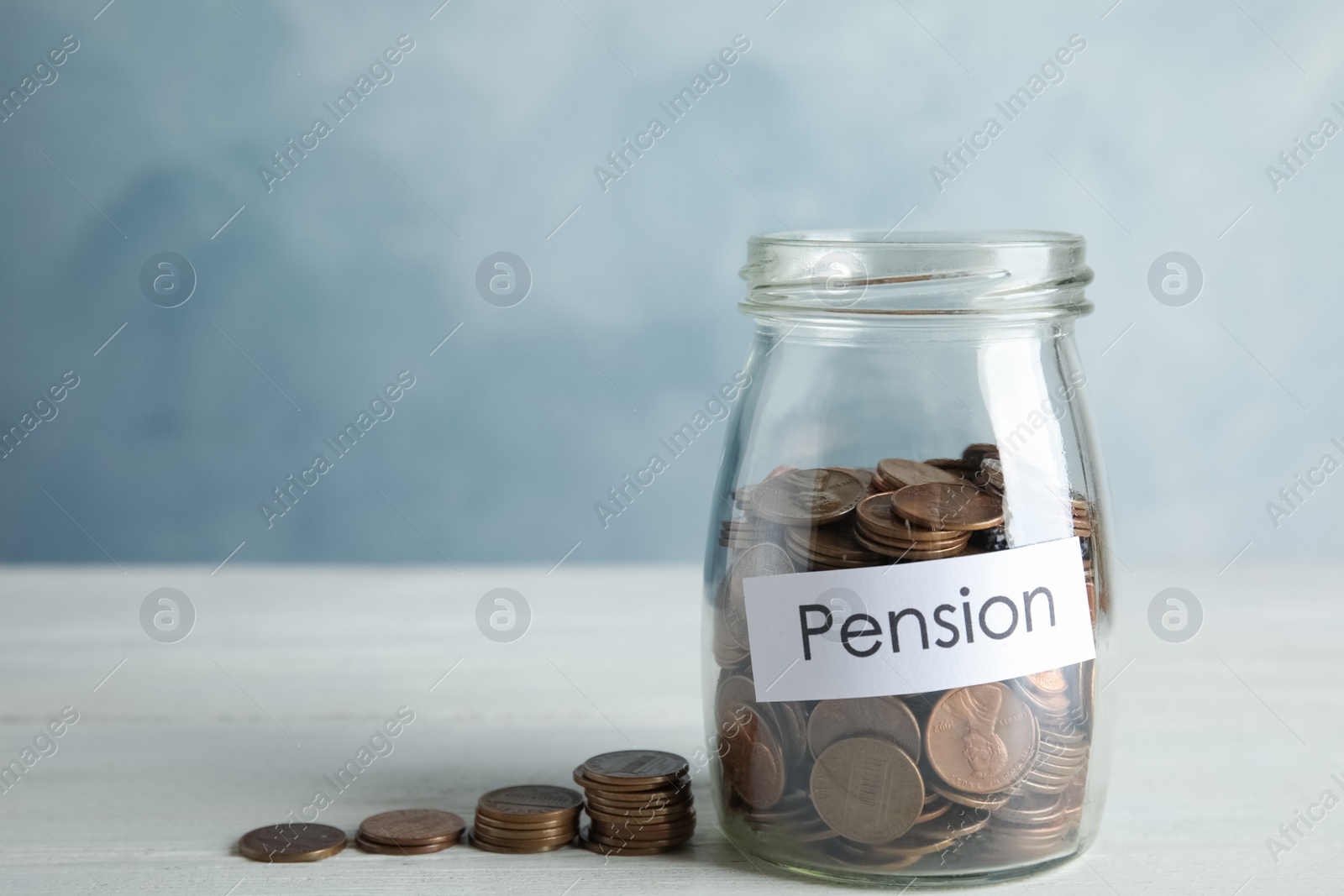 Photo of Glass jar with label PENSION and coins on white table. Space for text