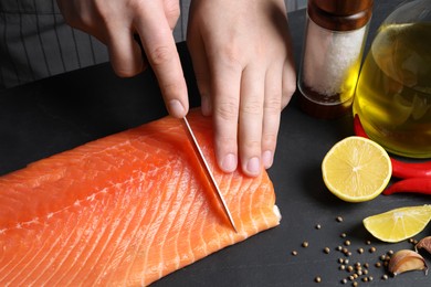 Photo of Man cutting raw salmon at black table, closeup