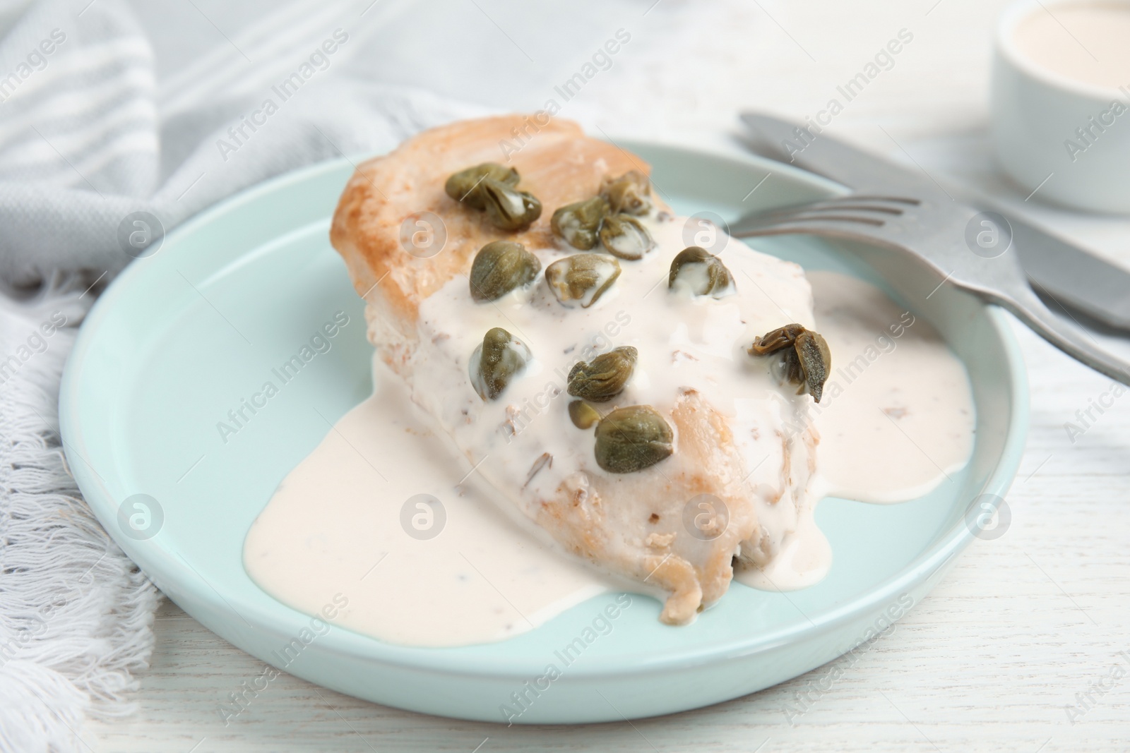 Photo of Delicious cooked chicken fillet with capers and sauce served on white wooden table, closeup