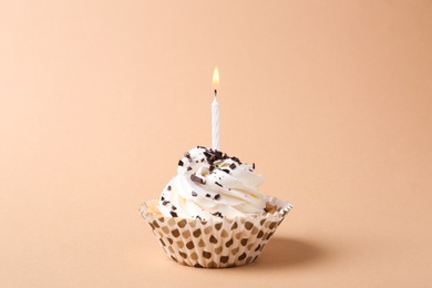 Photo of Delicious birthday cupcake with candle on beige background