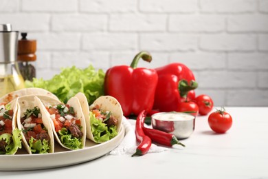 Delicious tacos with meat and vegetables on white table against light brick wall, closeup