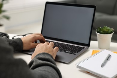 Photo of E-learning. Young man using laptop at white table indoors, closeup