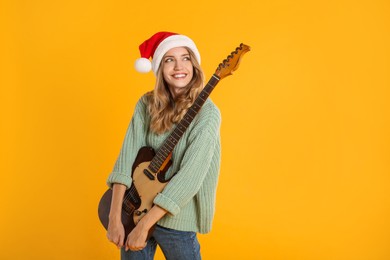 Photo of Young woman in Santa hat with electric guitar on yellow background, space for text. Christmas music