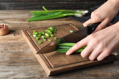 Photo of Woman cutting fresh green onion on wooden board at table, closeup