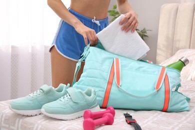 Photo of Woman packing sports stuff for training into bag at home, closeup