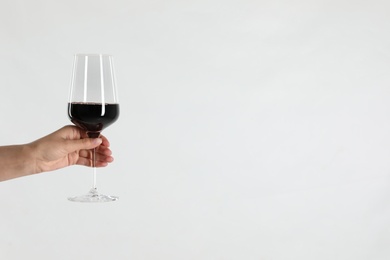 Woman holding glass of red wine on light background, closeup. Space for text