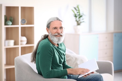 Photo of Handsome mature man reading book on sofa, indoors