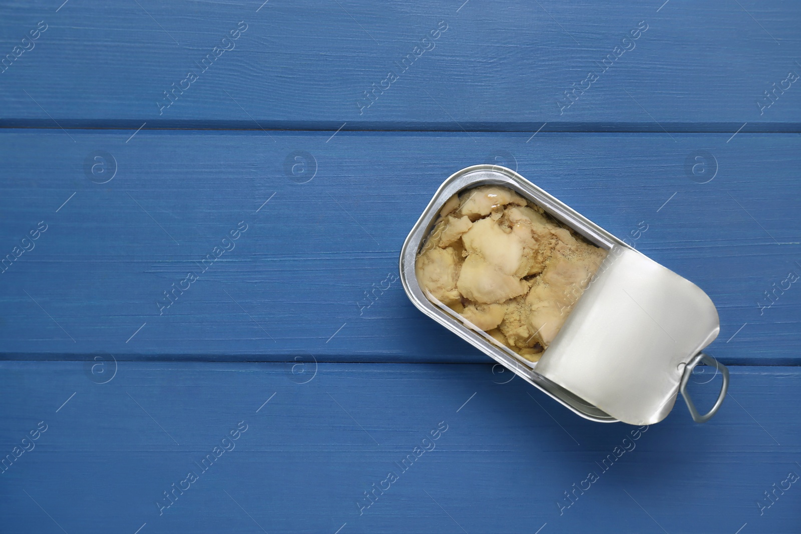 Photo of Open tin can of tasty cod liver on blue wooden table, top view. Space for text