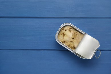 Open tin can of tasty cod liver on blue wooden table, top view. Space for text