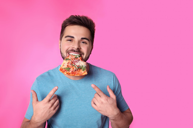 Handsome man eating pizza on pink background