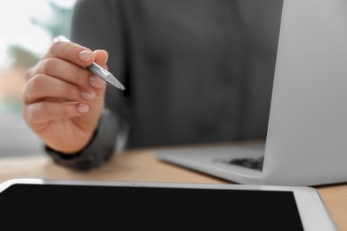 Woman with tablet and pen working on laptop at wooden table, closeup. Electronic document management