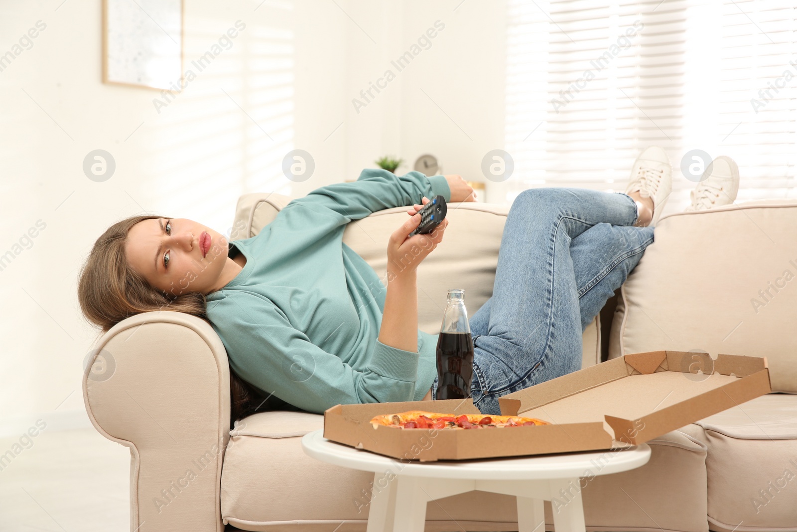 Photo of Lazy young woman with pizza and drink watching TV at home