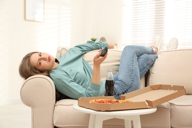 Lazy young woman with pizza and drink watching TV at home