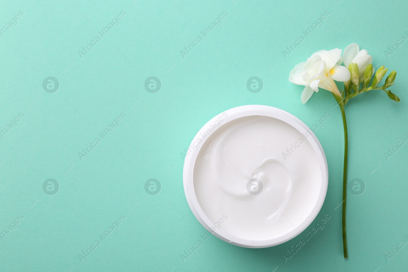 Photo of Moisturizing cream in open jar and freesia flower on turquoise background, flat lay with space for text. Body care product