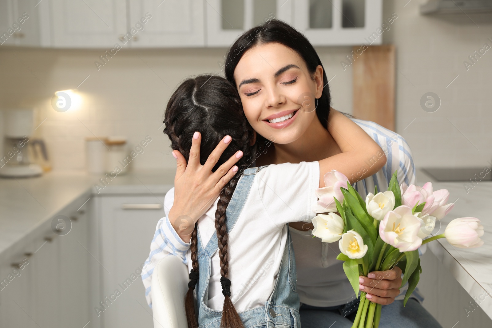 Photo of Little daughter congratulating her mom in kitchen at home. Happy Mother's Day