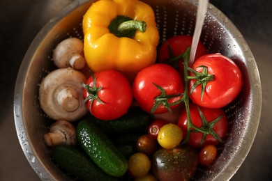 Photo of Washing different vegetables with tap water in metal colander inside sink, top view