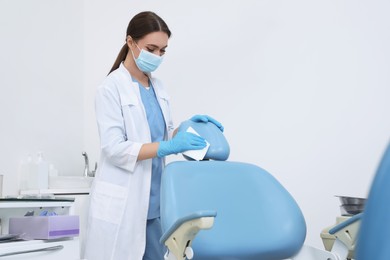 Professional dentist in white coat and medical mask cleaning workplace indoors