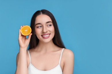 Beautiful young woman with piece of orange on light blue background. Space for text