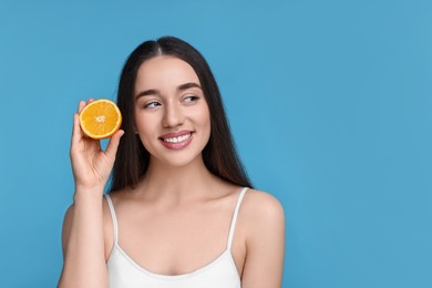 Photo of Beautiful young woman with piece of orange on light blue background. Space for text