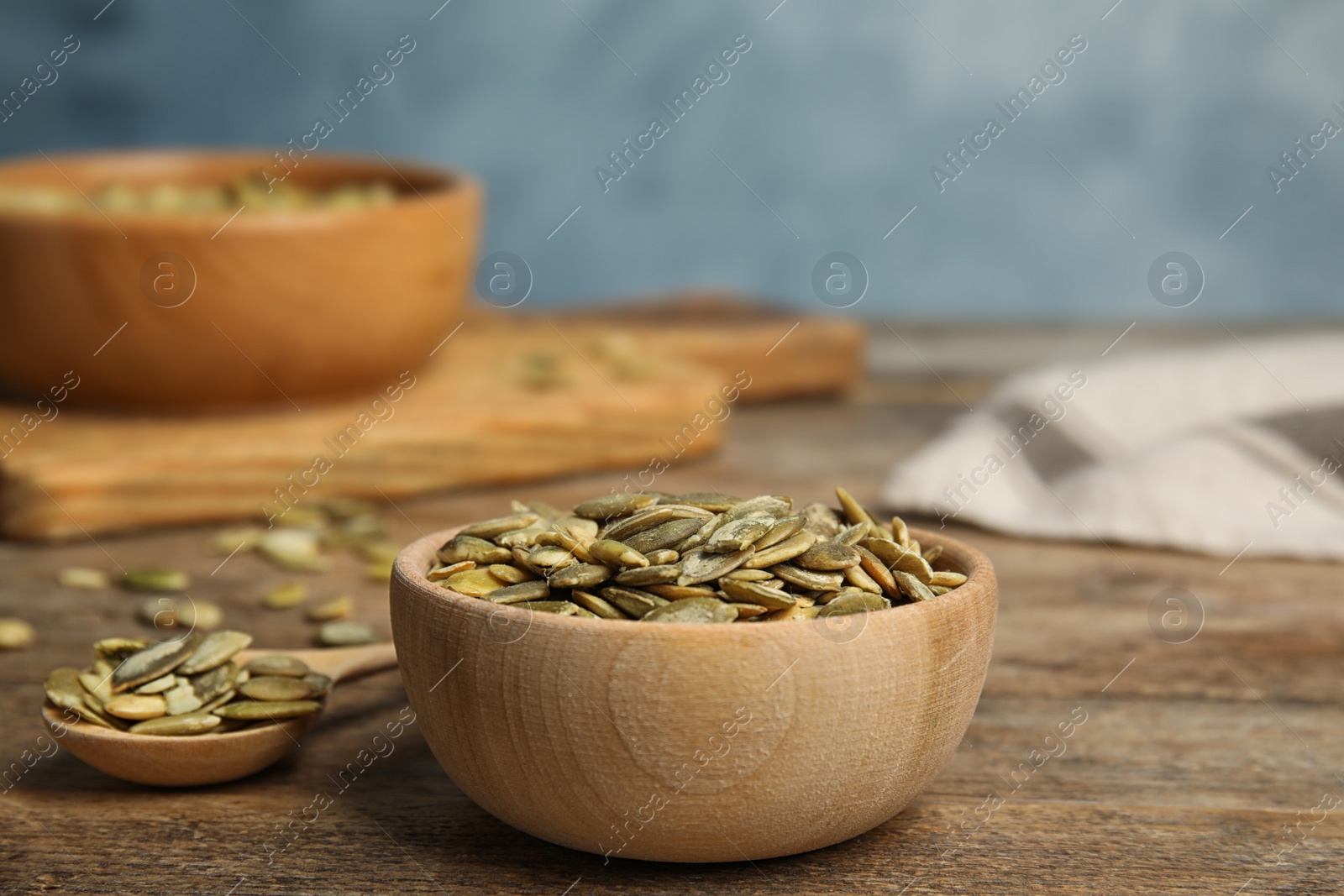 Photo of Bowl and spoon of raw peeled pumpkin seeds on wooden table. Space for text