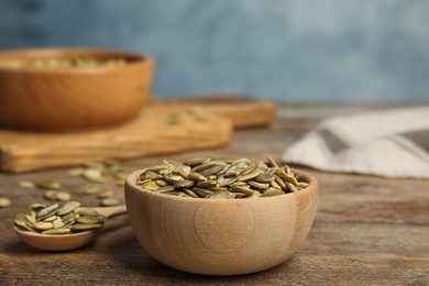 Photo of Bowl and spoon of raw peeled pumpkin seeds on wooden table. Space for text