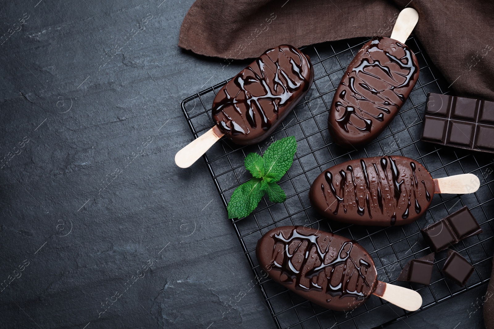 Photo of Delicious glazed ice cream bars, chocolate and mint on black table, flat lay. Space for text