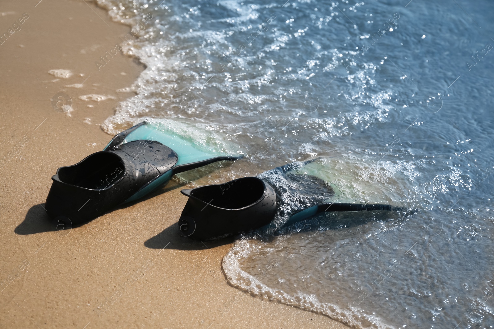 Photo of Pair of turquoise flippers on sand near sea